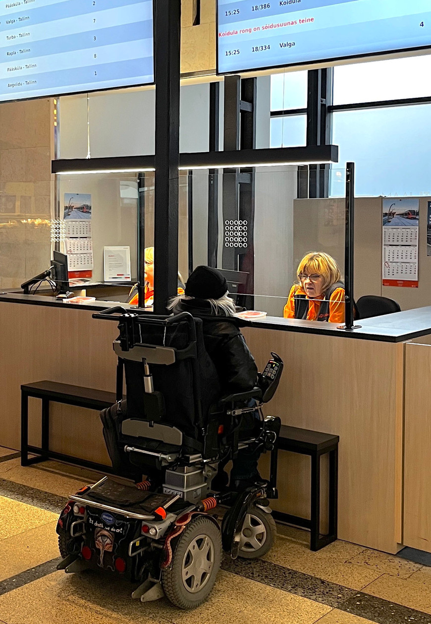 A wheelchair user receiving assistance at a railway station information desk